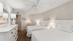 A hotel room with two beds, a ceiling fan, a dresser, and bedside lamps.