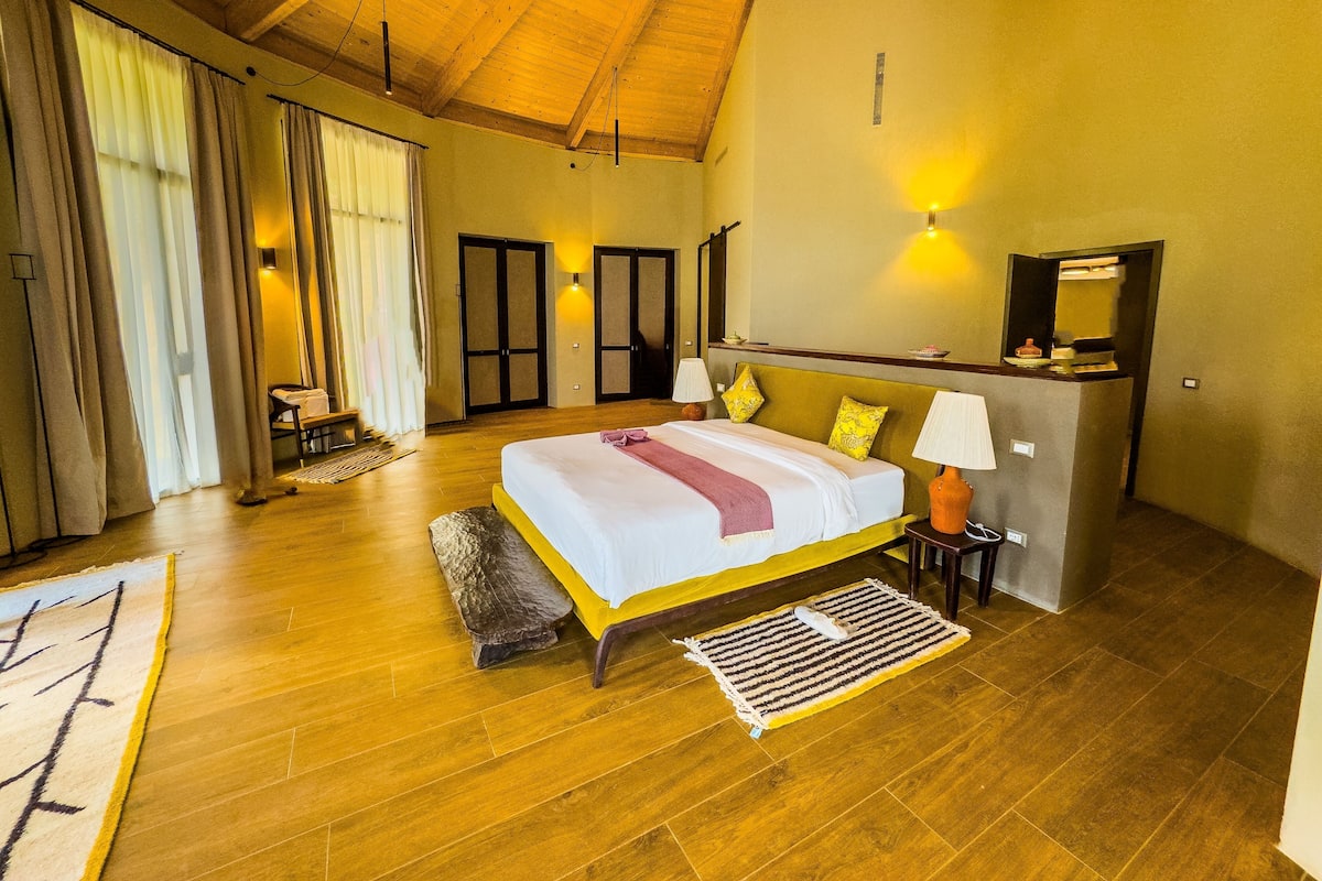 Ein geräumiges Schlafzimmer mit einem großen Bett, Holzboden und hoher Decke.