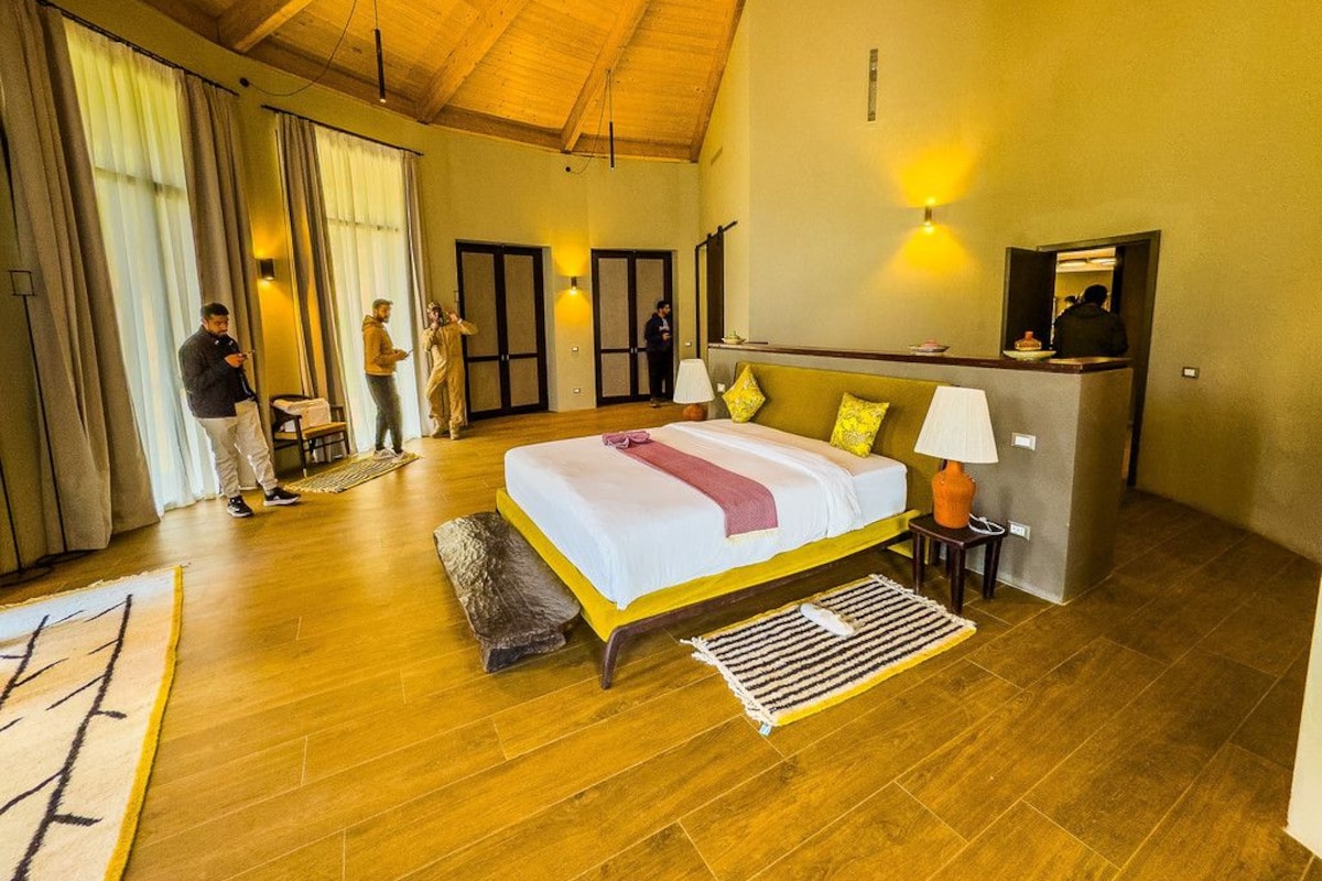 A spacious bedroom with a large bed, wooden flooring, and a high ceiling.