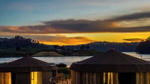 Una hilera de casas de campo con techos de paja, con vistas a un lago y colinas al atardecer.