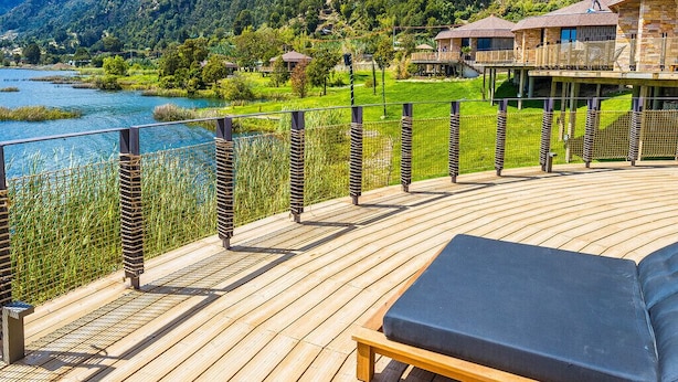 Una terraza de madera con zona de estar, con vista a un lago y colinas boscosas.