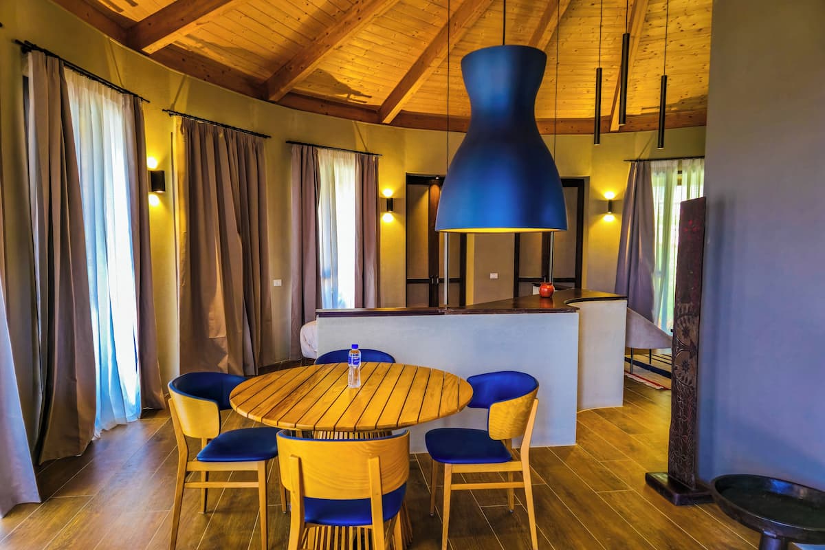 Ein Essbereich mit einem runden Holztisch, sechs Stühlen und einer blauen Pendelleuchte.