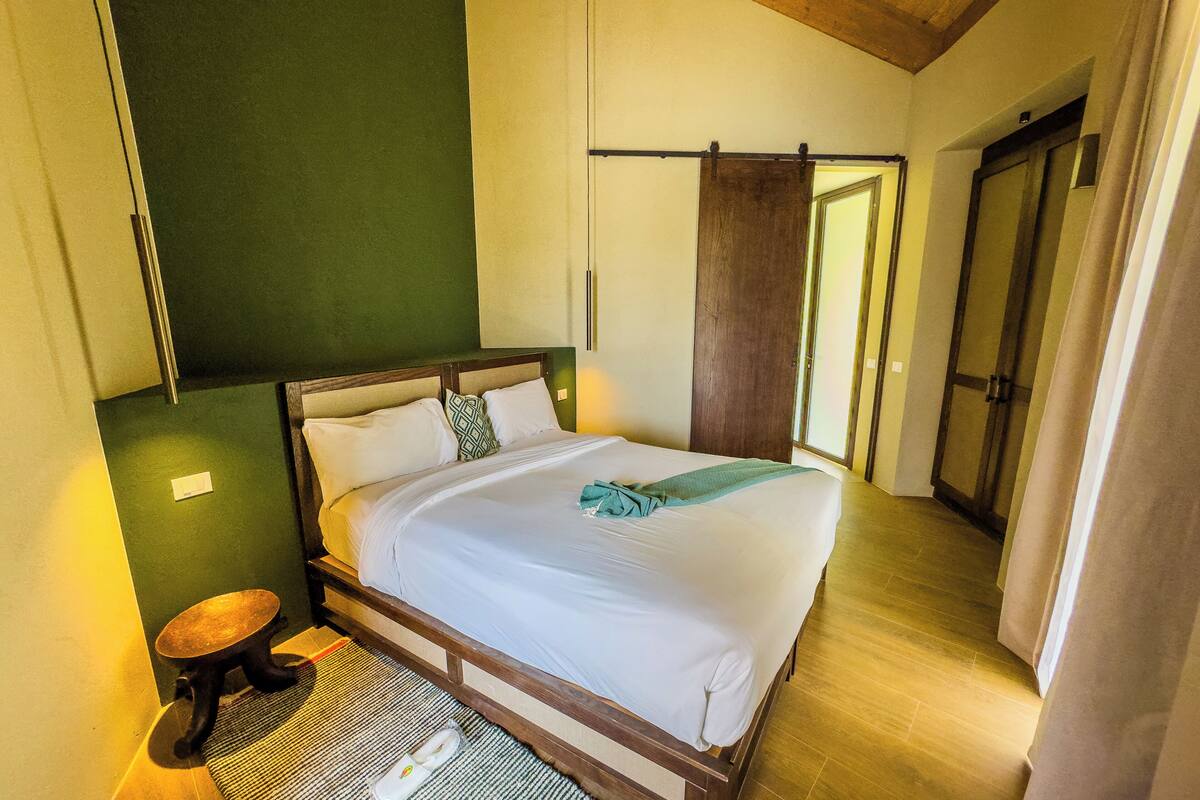 Ein ordentlich gemachtes Bett in einem Zimmer mit einem hölzernen Kopfteil, einem kleinen runden Tisch und einer grünen Wand.
