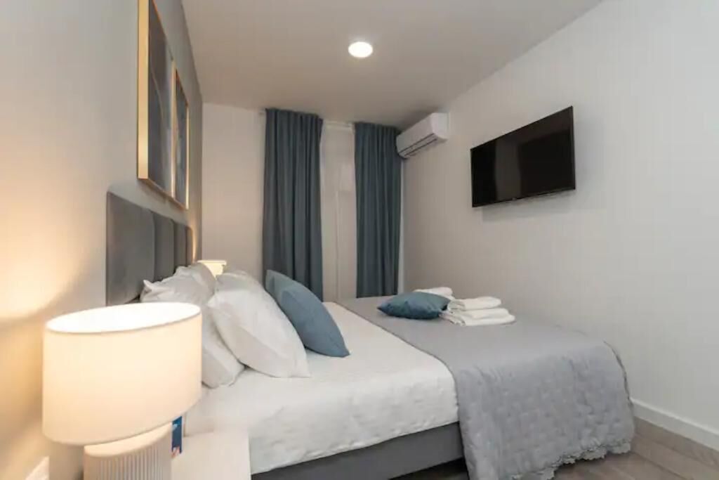 Una habitación de hotel moderna con cama, televisor de pantalla plana en la pared y ventana con cortinas.