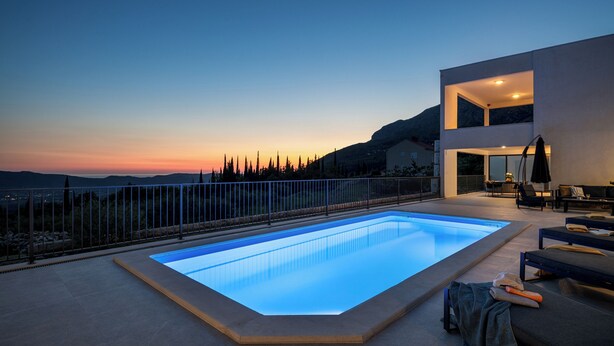 Une piscine extérieure moderne offrant une vue sur le coucher de soleil et les montagnes en arrière-plan.