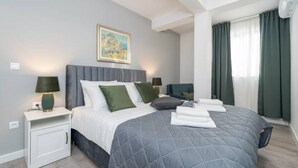 Une chambre d’hôtel moderne avec un grand lit, deux tables de chevet, un tableau au mur et une fenêtre avec des rideaux.