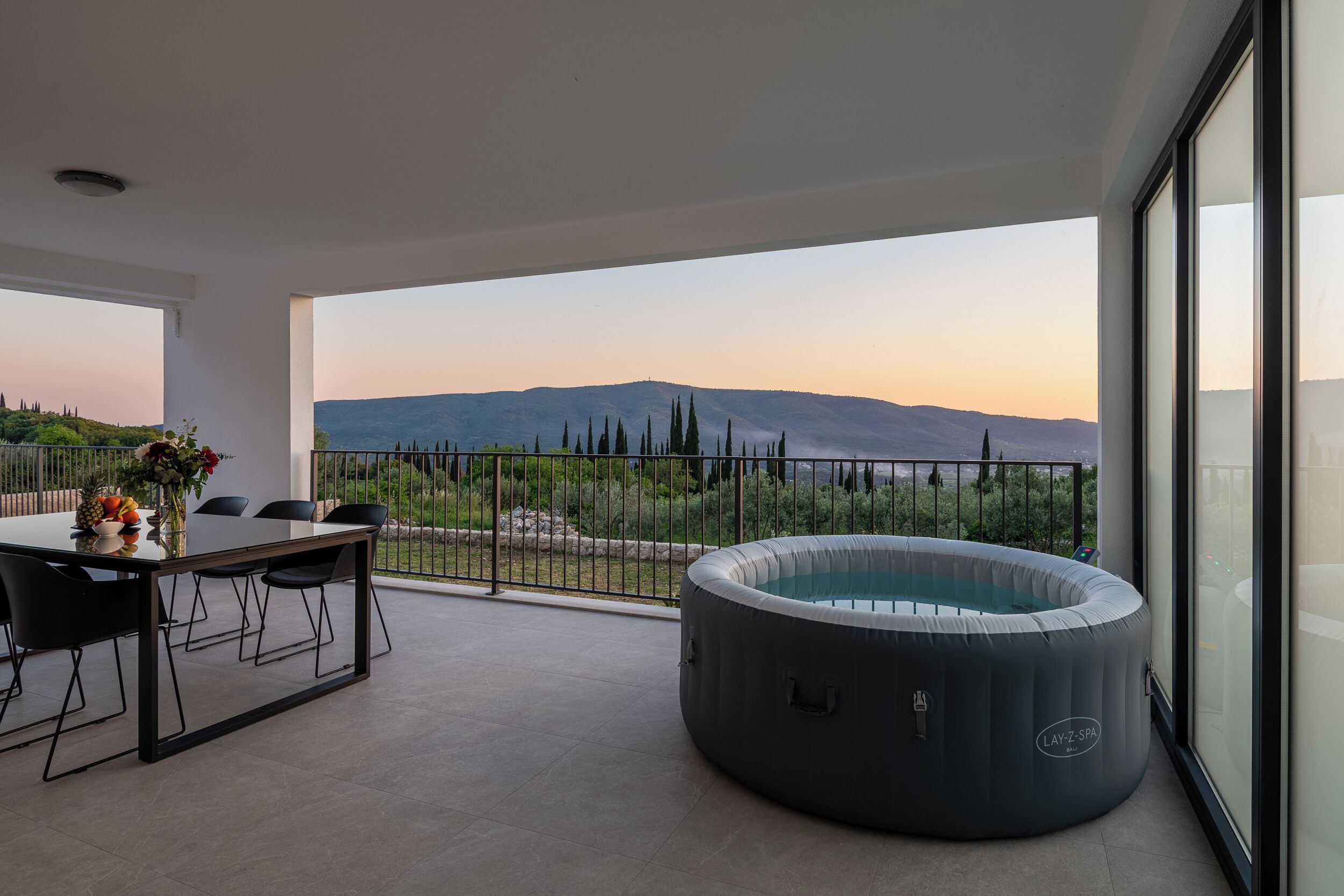 Un balcón con hidromasaje, mesa de comedor y sillas, con vista a un paisaje montañoso.