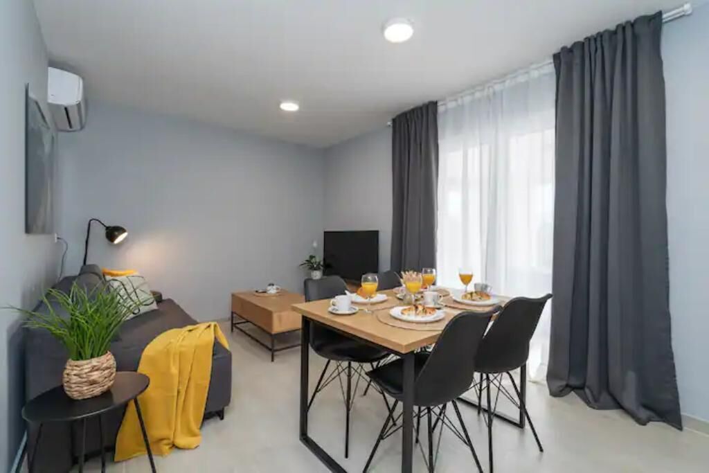 Ein modernes Wohnzimmer mit einer Couch, einem Esstisch für zwei Personen, einem Fernseher und einer Pflanze.