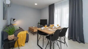Un salon moderne avec un canapé, une table à manger dressée pour deux personnes, un téléviseur et une plante.
