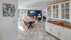 A dining area with a table set for four, surrounded by chairs, a kitchen area with cabinets, and a blue wall in the background.