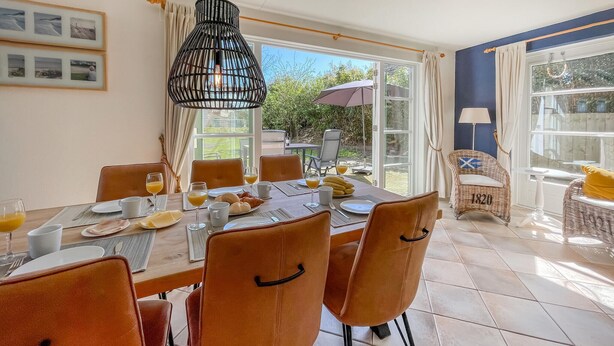 A dining area with a table set for breakfast, chairs, a hanging light fixture, and a view of the outdoors.