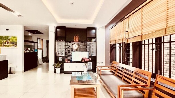A modern living room with a sofa, wooden chairs, a glass coffee table, and a kitchen area in the background. - Pearl Beach Homestay (Da Nang)