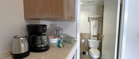 Una cocina con cafetera, tetera y utensilios, y un baño con inodoro y lavabo.