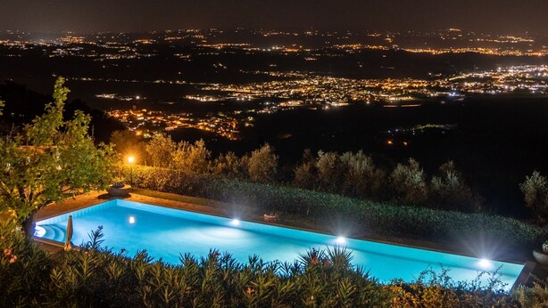 A nighttime view of a cityscape with a swimming pool in the foreground. - Country House in Touscany ID 4161 (Buti)