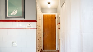 A narrow hallway with a wooden door, a white tiled wall with red trim, a light fixture, and a framed picture. - Acreage Near Downtown (Indianapolis)