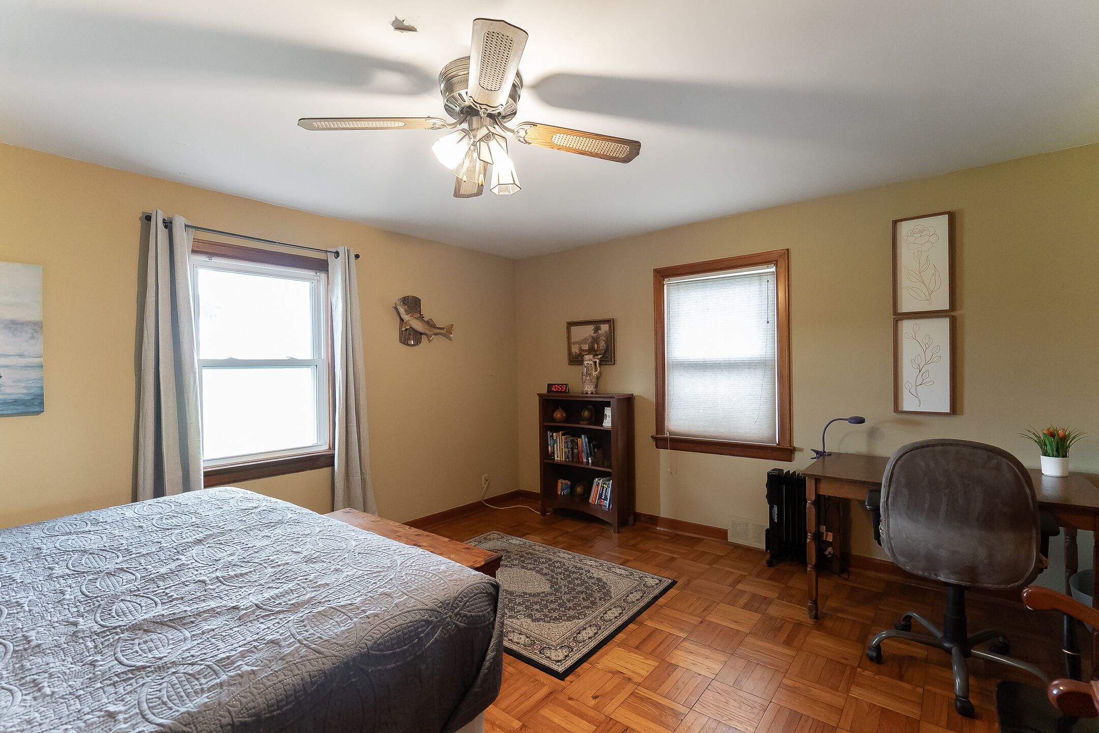 Une chambre à coucher comprenant un lit, un bureau, une chaise, une bibliothèque et un ventilateur de plafond.