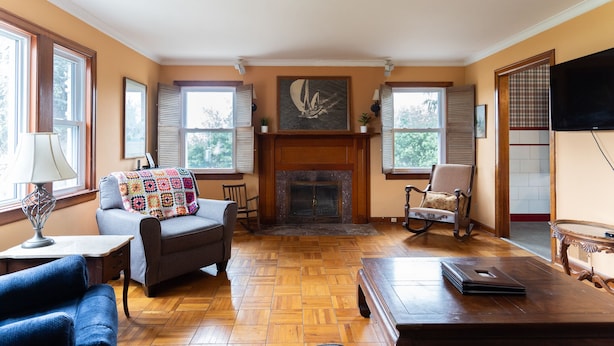 A living room with a fireplace, wooden flooring, a ceiling fan, and a television. - Acreage Near Downtown (Indianapolis)