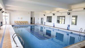 Une grande piscine intérieure à l’eau d’un bleu limpide, avec des murs et un sol carrelés.