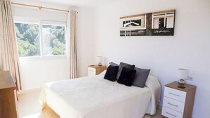 Une chambre avec un grand lit, deux tables de chevet, une fenêtre avec des rideaux et une œuvre d’art accrochée au mur.