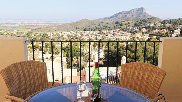 Un balcon avec des fauteuils et une table en osier, donnant sur une ville avec une montagne en arrière-plan.
