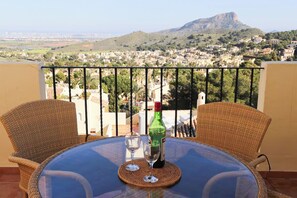 Ein Balkon mit Korbstühlen und einem Tisch, der auf eine Stadt mit einem Berg im Hintergrund blickt.
