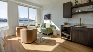 A modern living room with a sofa, armchairs, a TV, and a kitchen area with a sink and cabinets. - The Georgie Studio/1Bath Located in the heart of Downtown (Sitka)