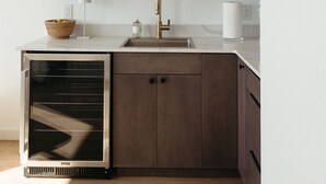 A modern kitchen with dark wooden cabinets, a white countertop, and a built-in dishwasher. - The Georgie Studio/1Bath Located in the heart of Downtown (Sitka)