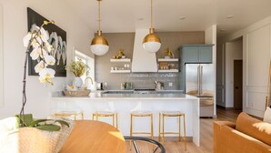 A modern kitchen with a central island, pendant lights, and a dining area with a wooden table and bar stools. - The Ressa 2BED/1BATH Located in the heart of Downtown (Sitka)