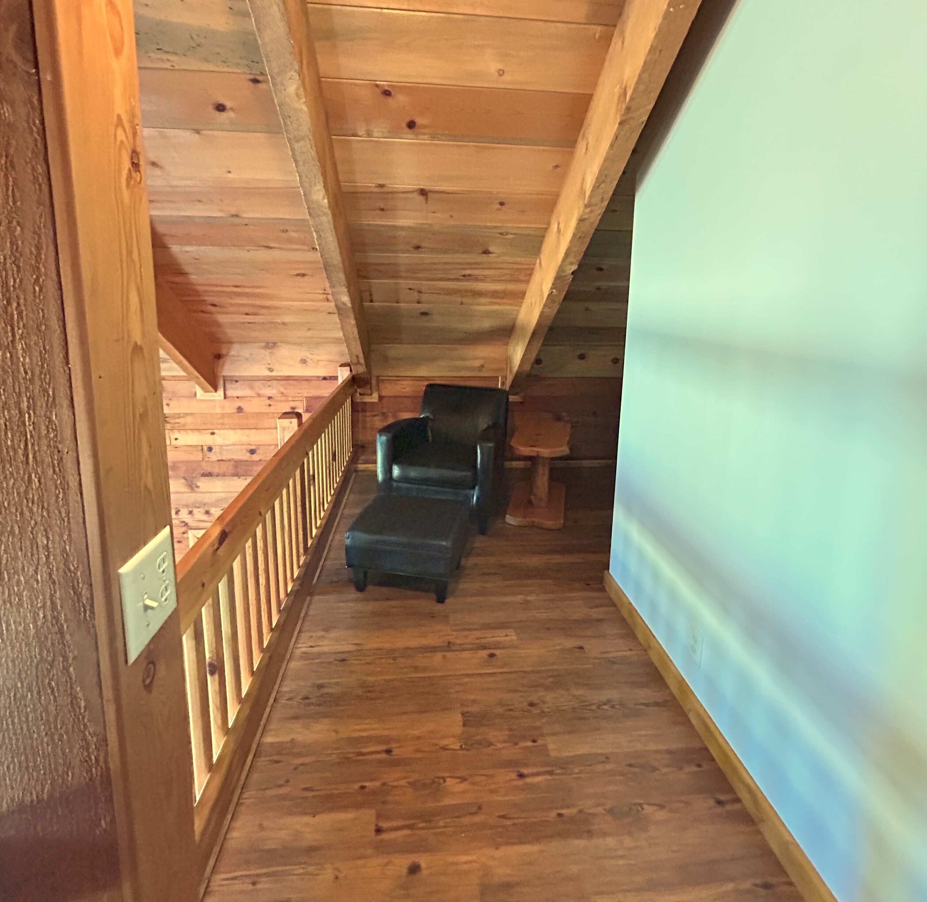 Una escalera de madera que lleva a un dormitorio tipo loft con una cama, una silla y una pequeña mesa.