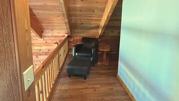 Una escalera de madera que lleva a un dormitorio tipo loft con una cama, una silla y una pequeña mesa.