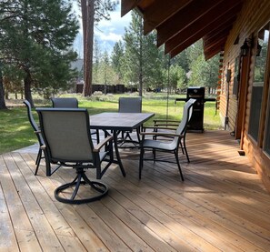 A wooden deck with a table and chairs, a grill, and a view of a forested area. - Cozy 3 bedroom, 3 bathroom, Log Home, PET FRIENDLY, Tollgate (Sisters)