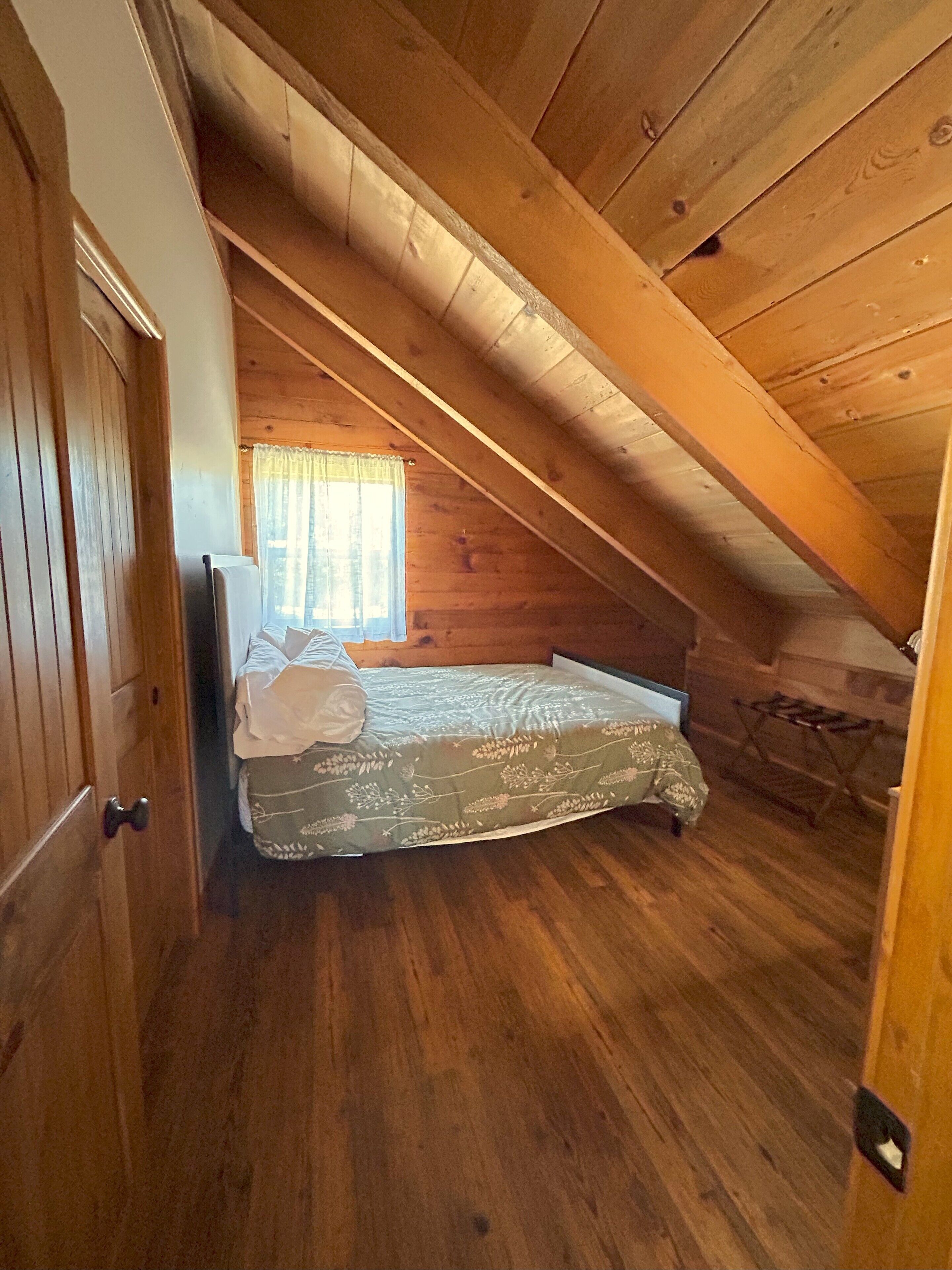 A small, cozy attic bedroom with wooden walls and a sloped ceiling.