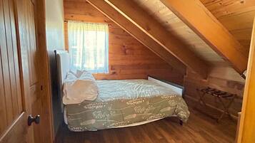 A small, cozy attic bedroom with wooden walls and a sloped ceiling.