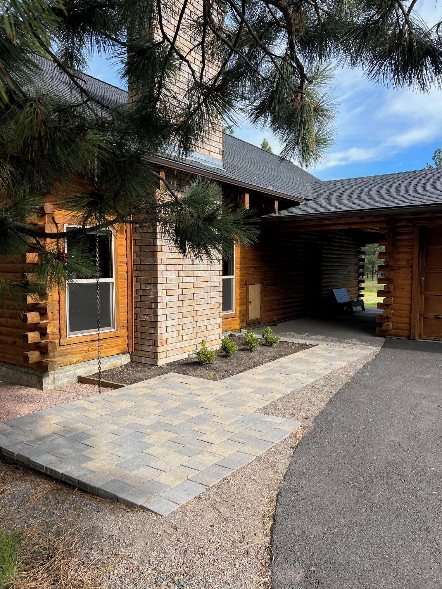 A log cabin with a stone foundation, a covered porch, and a gravel driveway.