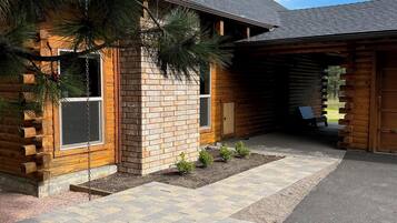 A log cabin with a stone foundation, a covered porch, and a gravel driveway.