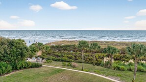 A coastal view with a pathway leading to a building, surrounded by lush greenery and palm trees.