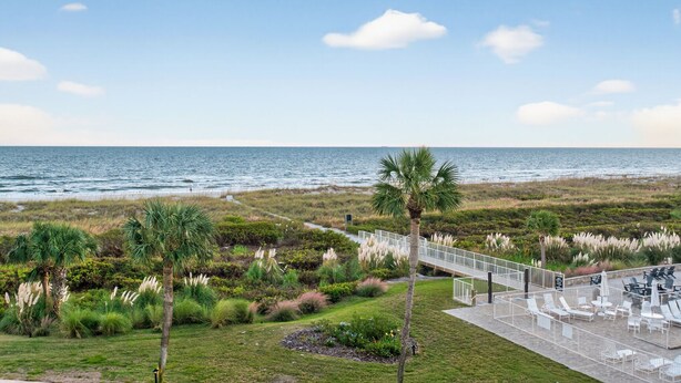 A coastal view with a pathway leading to a deck with outdoor seating overlooking the ocean.