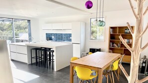 A modern kitchen with a central island, a dining area with yellow chairs, and a wooden tree sculpture.