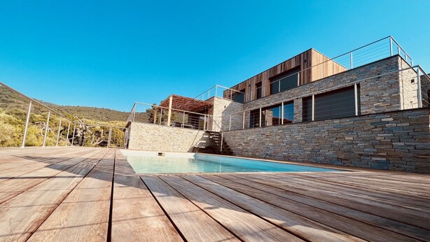 A modern house with a stone exterior, a wooden deck, and a swimming pool.