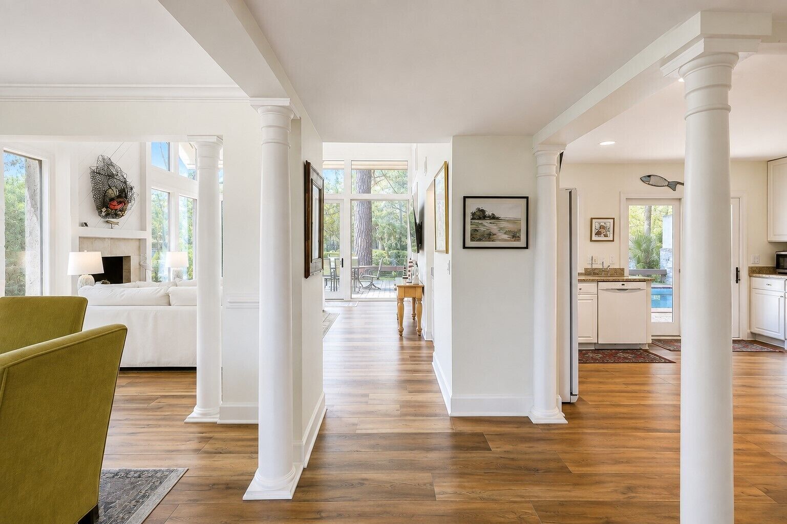 Un pasillo amplio con piso de madera, columnas blancas y vista a un comedor con mesa y sillas.