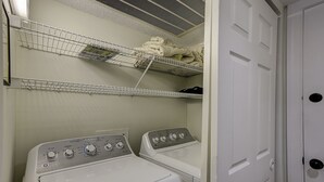 A laundry room with two stacked washing machines and two wire shelves above them. - 30 Windjammer - Take in the Back Nine Views of Harbour Town Golf Links (Hilton Head Island)