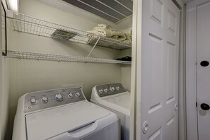 A laundry room with two stacked washing machines and two wire shelves above them. - 30 Windjammer - Take in the Back Nine Views of Harbour Town Golf Links (Hilton Head Island)