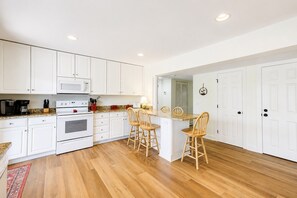 A kitchen with white cabinets, a microwave, an oven, and a dining area with wooden chairs.