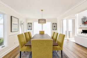 Een eetkamer met een lange tafel, zes stoelen en een kroonluchter.