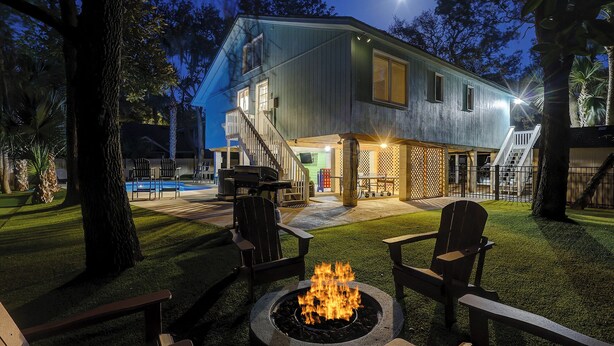 A two-story house with a fire pit in the backyard, surrounded by outdoor seating and a pool. - 78 Dune Lane - 2nd Row Ocean Home in NFB with Backyard Entertainment! (Hilton Head Island)
