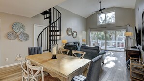 A spacious living area with a wooden dining table, a dark-colored sofa, and a spiral staircase. - 78 Dune Lane - 2nd Row Ocean Home in NFB with Backyard Entertainment! (Hilton Head Island)