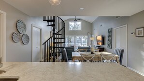 A spacious kitchen with a marble countertop, a dining area with a wooden table and chairs, a black spiral staircase, and a large window providing a view of the outdoors. - 78 Dune Lane - 2nd Row Ocean Home in NFB with Backyard Entertainment! (Hilton Head Island)