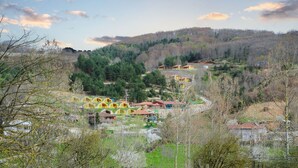 Zona rural con un conjunto de edificios amarillos y rojos, rodeada de bosques densos y colinas.
