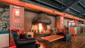 Un rincón interior acogedor con pared de ladrillo, una chimenea grande y una mesa de madera.