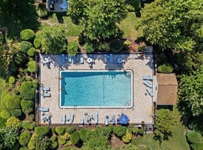 An aerial view of a rectangular swimming pool with lounge chairs and umbrellas, surrounded by well-maintained greenery. - Cozy Coastal Value – 2BR Sea Pines Townhome Just a Block from the Beach! (Bethany Beach)